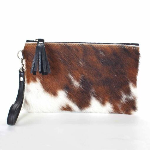 A brown and white cow print purse with black leather strap.