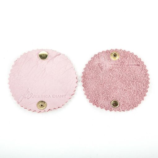 Two pink circular coasters with a gold metal holder.